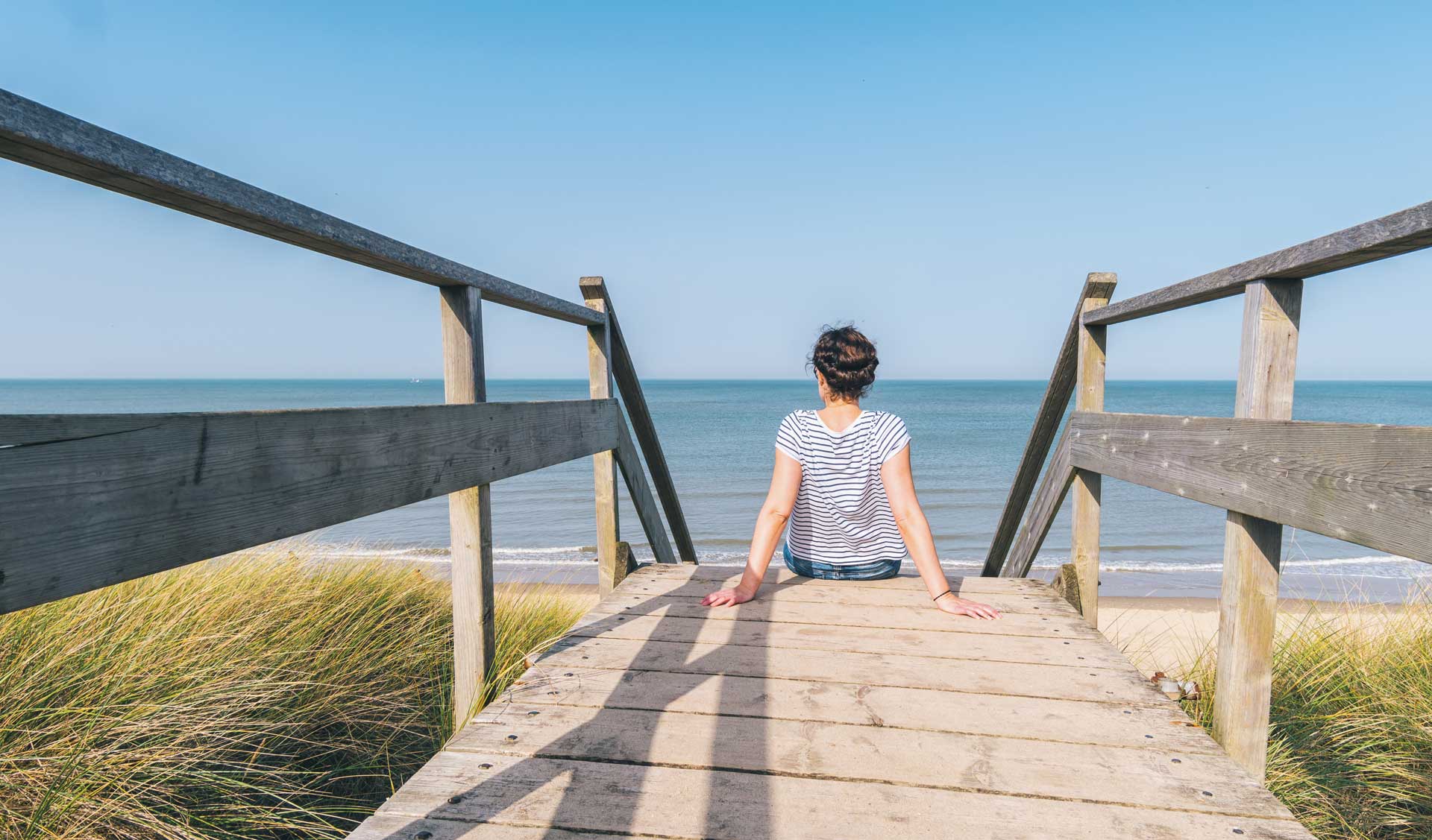 Frau sitzt auf einem Steg auf Sylt und schaut auf das Meer