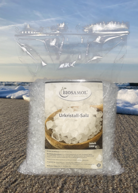Ein Nachfüllbeutel Ur-Kristallsalz von Biosamol, der vor einer Strand-Meer-Kulisse abgebildet ist
